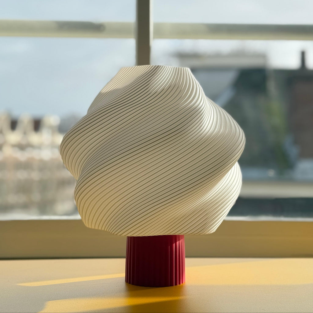 Decorative lamp with wavy design on a red base in front of a window