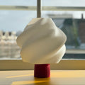 Decorative lamp with wavy design on a red base in front of a window