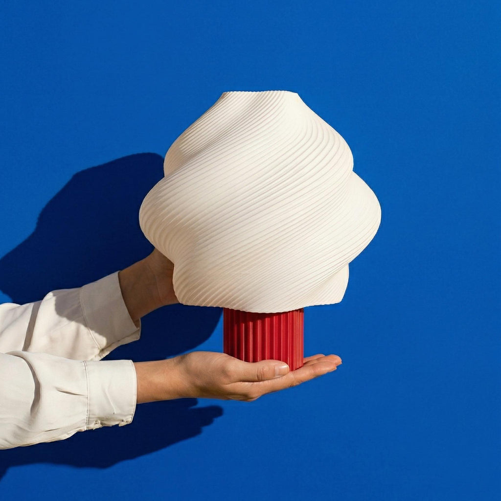 Person holding a large white ceramic vase with a red base against a blue background